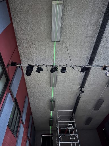 Ceiling lights and a green laser line above a metal scaffolding structure.