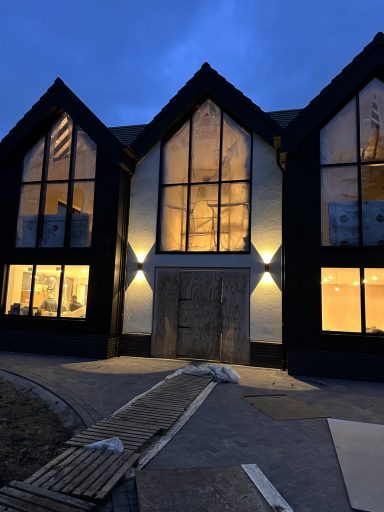 Modern black building with large windows illuminated at dusk.