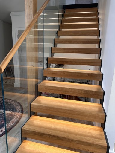 Stairs with wooden treads, glass railing, and warm lighting.