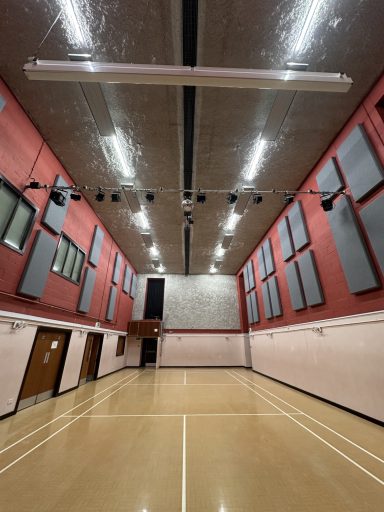 Interior of a gymnasium, featuring high ceilings, wooden floors, and wall-mounted sound panels.