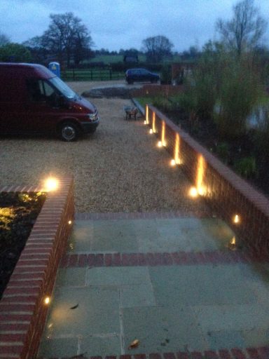 Pathway with ground lighting, gravel surface, red van, and green landscape in dusk light.