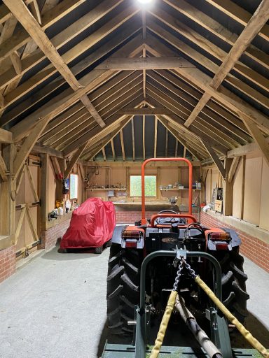 Interior of a rustic barn featuring a tractor and covered vehicle under wooden beams.