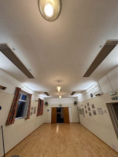 Interior of a spacious room with wooden floors, ceiling lights, and framed pictures on the walls.