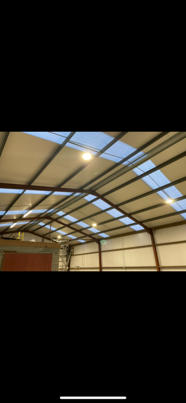 Interior view of a building showing a metal roof structure and natural light.