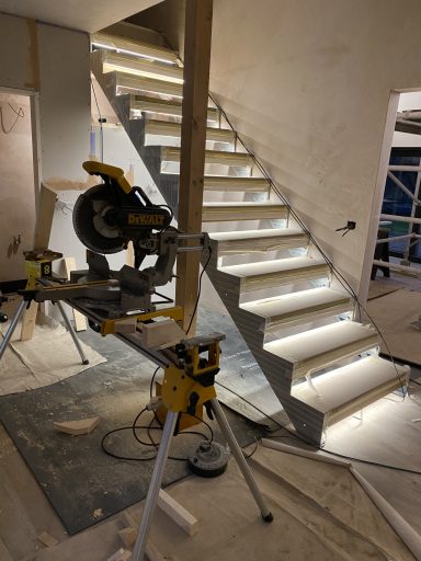 A mitre saw beside a staircase with illuminated steps under construction.