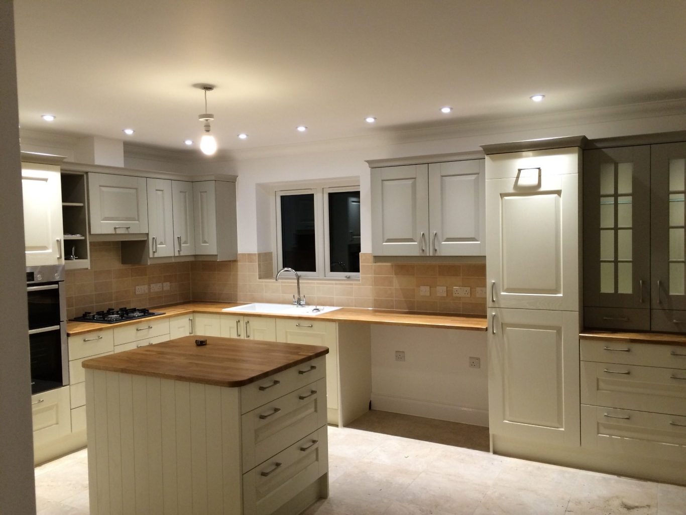 Modern kitchen with light-coloured cabinets, wooden countertop, and bright lighting, LED downlights, cupboard lighting and central lighting.