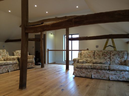 Spacious room with wooden beams and two patterned sofas. Natural light from large window.