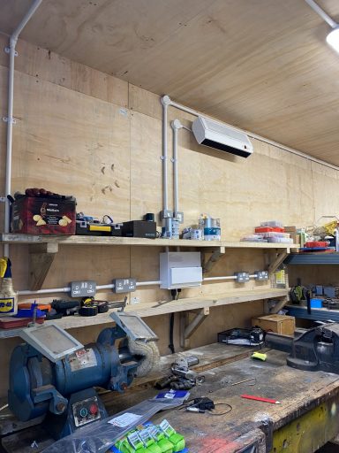 Cluttered workshop with tools and equipment on shelves and a workbench below.