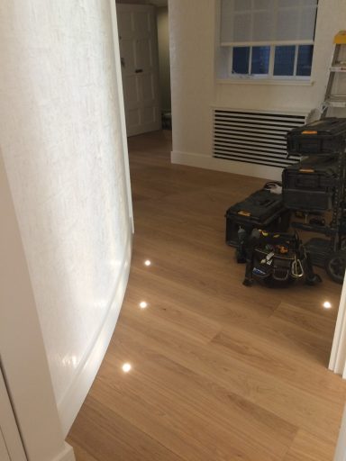 Light-coloured wooden flooring leads to a hallway with stacked tools in the background.