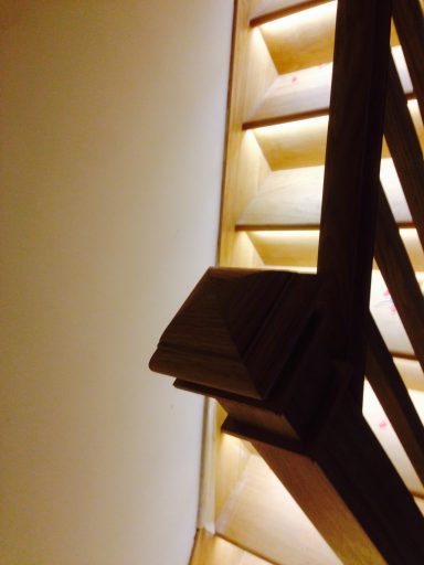 Wooden staircase with illuminated steps against a plain wall.