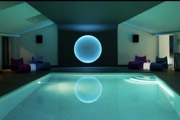 Indoor swimming pool with soft blue lighting and modern seating arrangements.