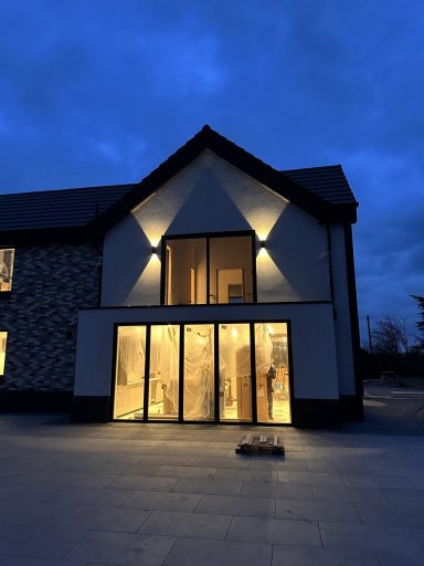 Modern house exterior at dusk, featuring large glass doors and soft lighting.