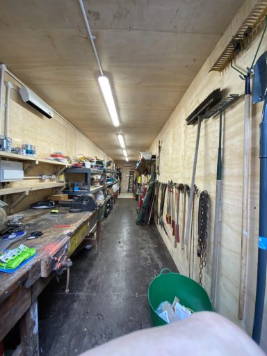 A long, narrow workshop with tools, shelves, and a green container along the walls.