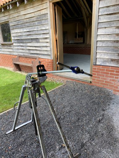 A workbench with a pipe vice outdoors beside a wooden structure.