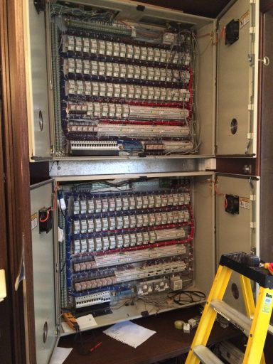 Electrical panel with multiple circuits and wiring, beside a ladder and workspace.