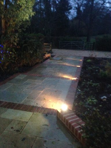 A dimly lit garden path lined with bricks and illuminated by subtle ground lights.