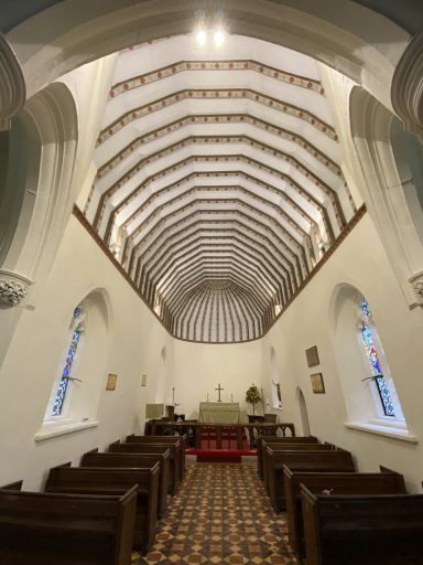 Interior of a church featuring a high, patterned ceiling and wooden pews.