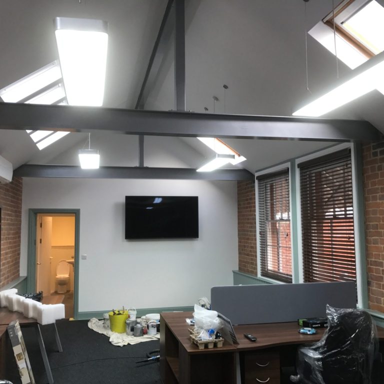 Modern office interior with hanging lighting, computer access points, and a wall-mounted television.