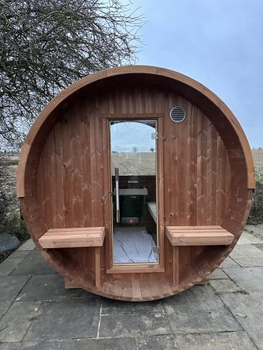 Round wooden sauna with benches and a central door, set against a cloudy sky.