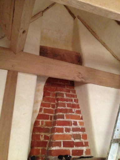 Exposed brick chimney with wooden beams in a rustic interior setting.