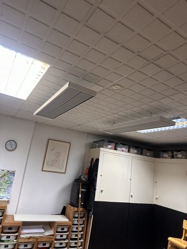 Ceiling with lights and storage cabinets in a room with a clock on the wall.