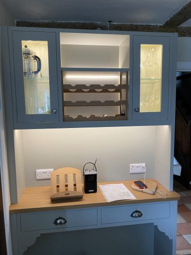 Light grey kitchen cabinet with glass doors, illuminated shelves, and wooden countertop.
