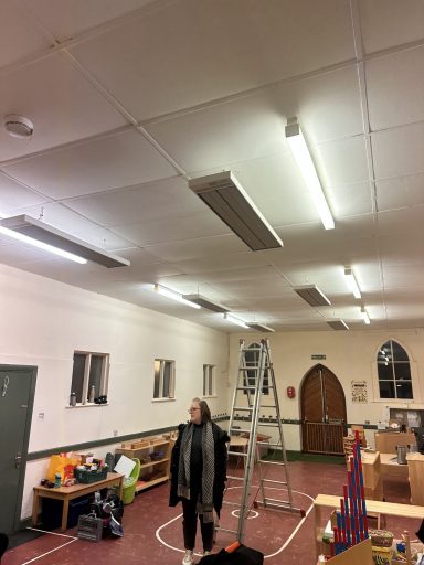 A person stands in a room with fluorescent lights, a ladder, and shelves.