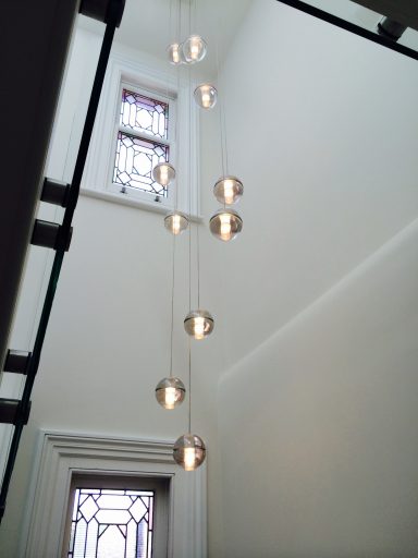 Modern pendant lights suspended in a stairwell with white walls and stained glass windows.