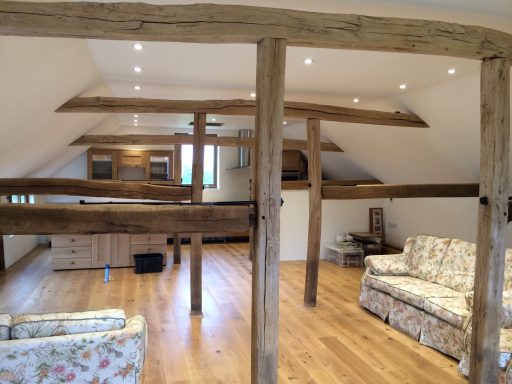 Spacious loft with wooden beams, two sofas, and wooden flooring.