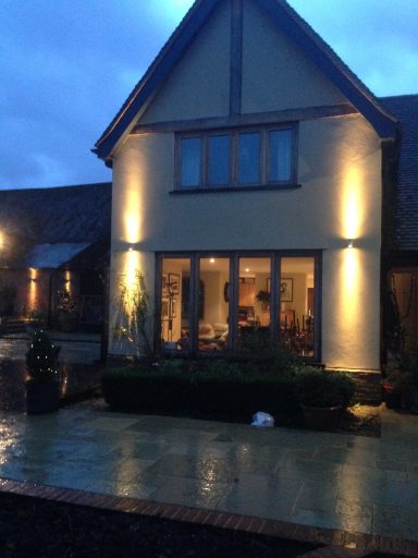 A modern house illuminated at dusk, with a landscaped garden and wet paving stones.