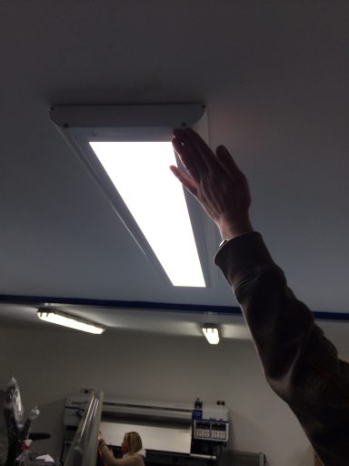 A hand reaching up to a ceiling-mounted LED light fixture.