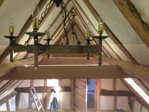 Wooden beams with a chandelier in a loft space, featuring a ladder and doorway.